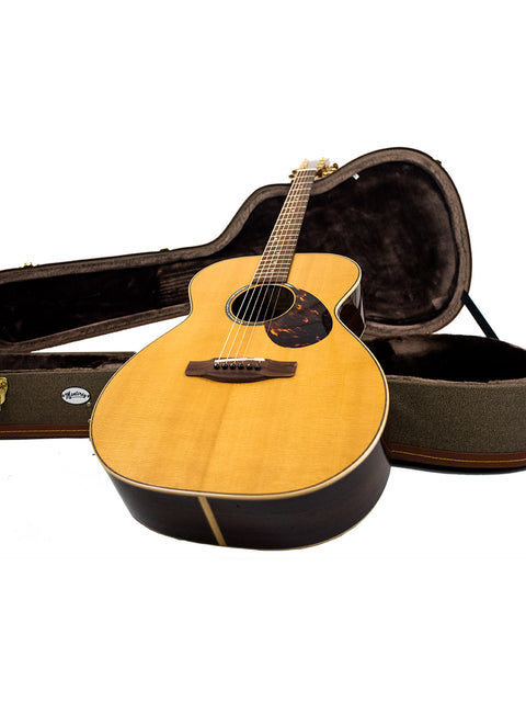 Gerard Gilet 000 14 Fret Acoustic guitar with its case, displayed against a clean white background, highlighting its beauty.
