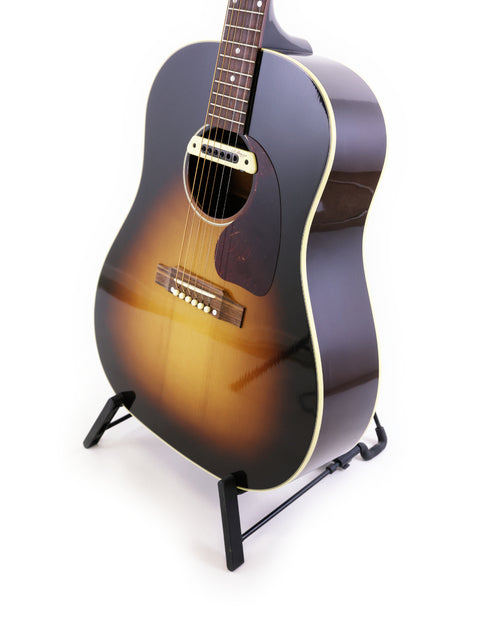 Gibson J-45 True Vintage guitar on a stand against a clean white background, showcasing its classic design.

