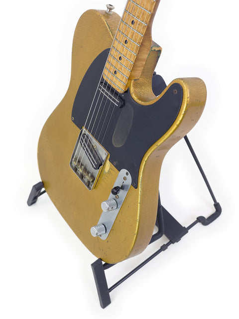 Gold-colored electric guitar with visible wear, on a black stand against a white background.