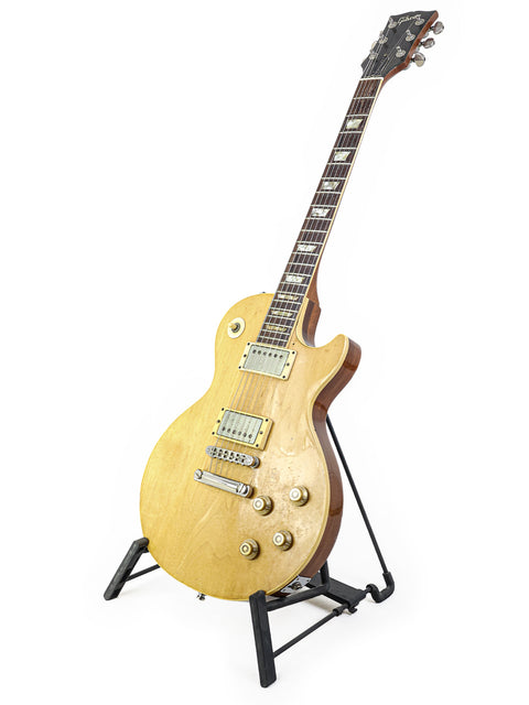 Golden 1973 Gibson Les Paul Deluxe guitar on a stand, set against a bright white backdrop.