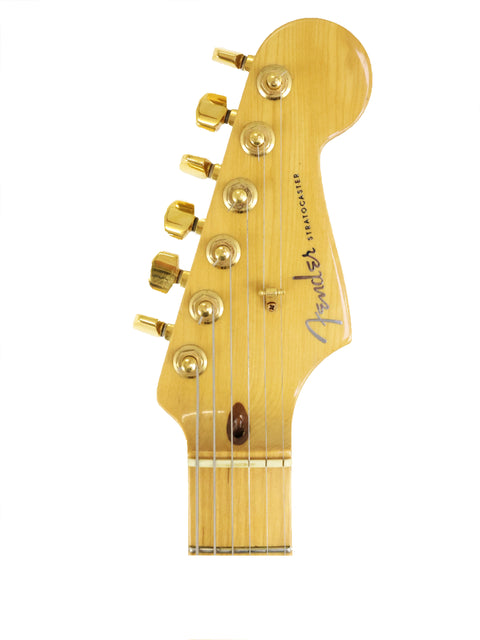 Headstock of a Fender Stratocaster guitar with gold tuners on white background.