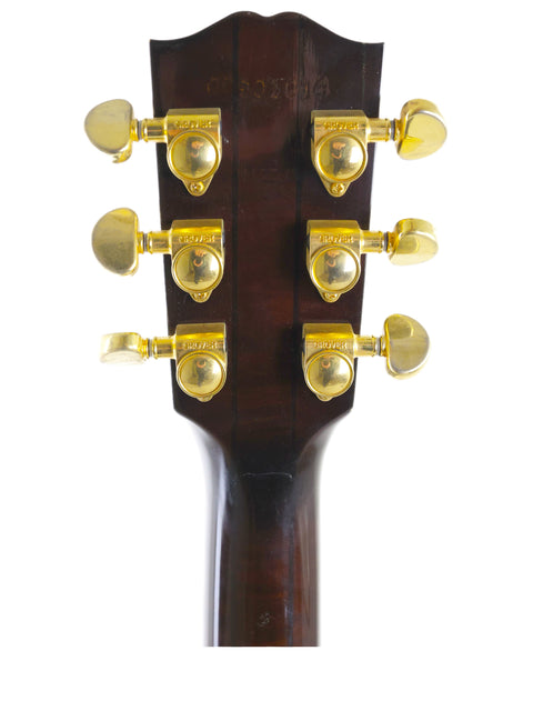 Headstock of a Gibson J-180EC acoustic guitar from 2001, featuring elegant gold hardware and intricate detailing.