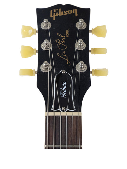 Headstock of a black-finished Gibson Les Paul Tribute electric guitar, showcasing its sleek design and craftsmanship.