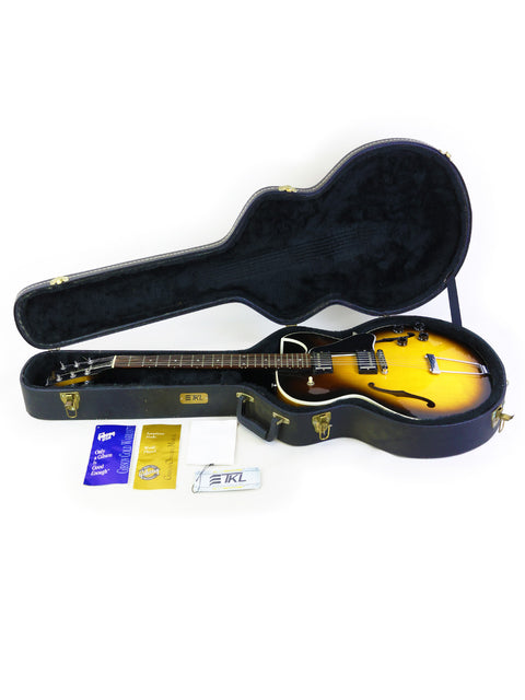 Inside a guitar case, a bright yellow Gibson ES-135 from 2001 is displayed, highlighting its unique design and color.