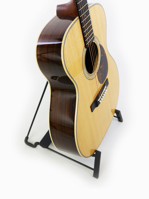 Martin 000-28 Modern Deluxe acoustic guitar displayed on a stand, highlighting its compact size and fine details.