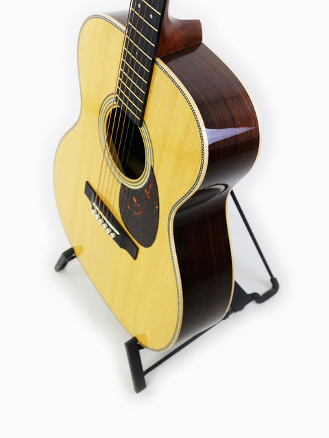 Martin 000-28 Modern Deluxe guitar displayed on a stand with a simple white backdrop.