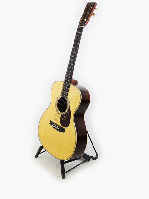 Martin 000-28 Modern Deluxe guitar displayed on a stand with a white backdrop.