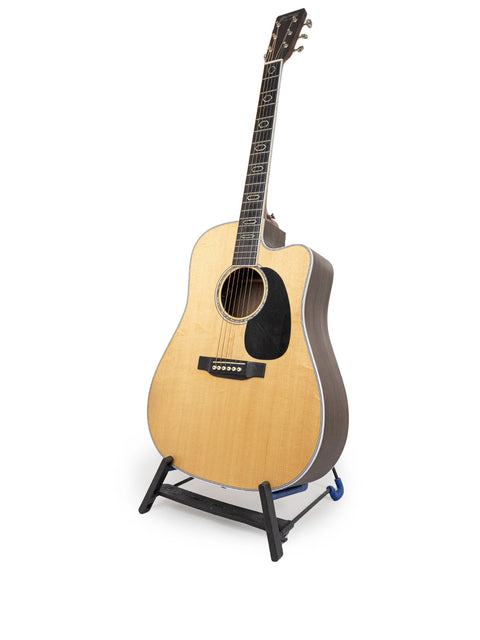 Martin DC Aura GT Dreadnought guitar on a stand, set against a clean white background, showcasing its elegant design.