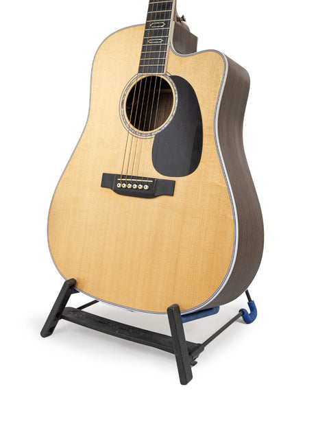 Martin DC Aura GT Dreadnought guitar rests on a stand against a clean white background, showcasing its elegant design.