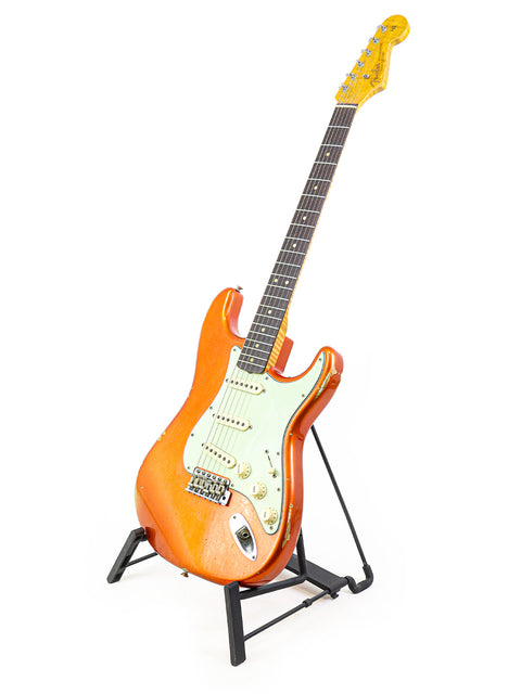 Orange Fender Ltd NAMM '64 Stratocaster Relic guitar displayed on a stand with a clean white backdrop.