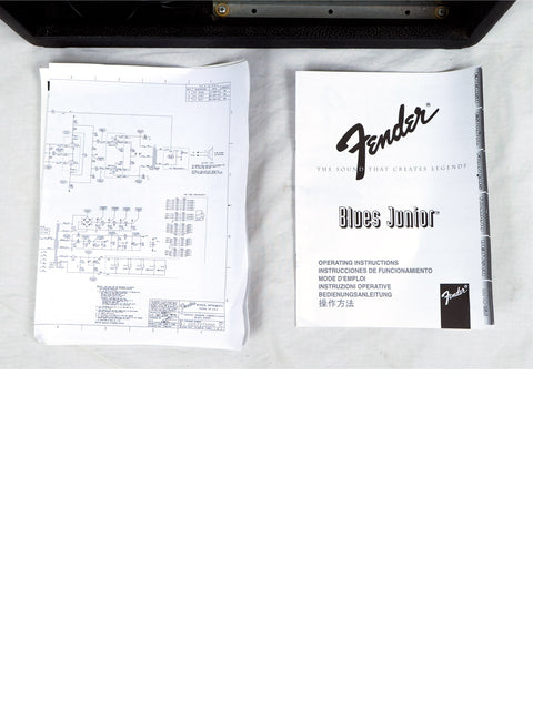 Schematic diagrams and a Fender Blues Junior manual on a black surface.