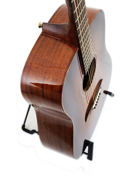 The Alvarez MDA66SHB guitar, crafted from wood, stands proudly on a stand with a bright white backdrop.
