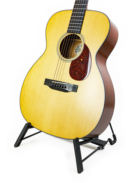 The Collings Julian Lage Signature OM1 guitar showcased on a stand, featuring a pristine white background.
