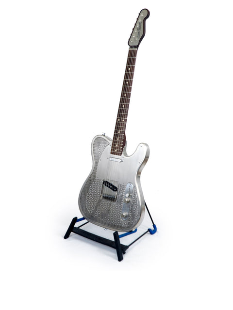 The James Trussart Holey Nickel Steelcaster, a silver guitar on a stand, elegantly presented with a white background.