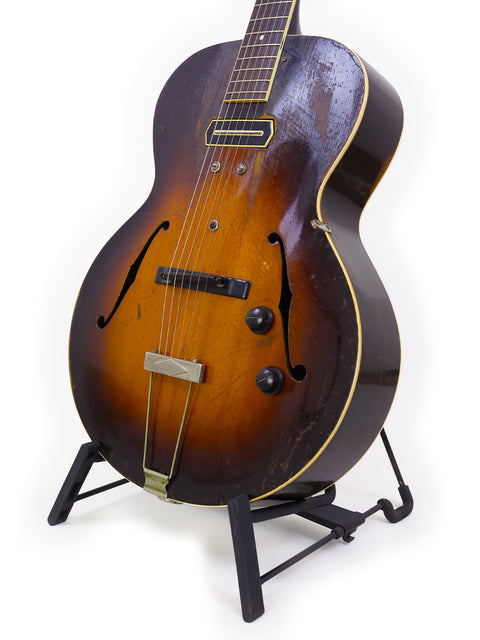 The image features a 1952 Gibson J-45 electric guitar, highlighting its iconic shape and craftsmanship, with a 1938 Gibson ES-150 nearby.