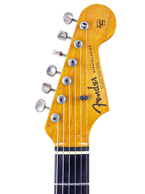 The photo presents a 1963 Fender L-Series Stratocaster, showcasing its striking black factory refin and legendary design.