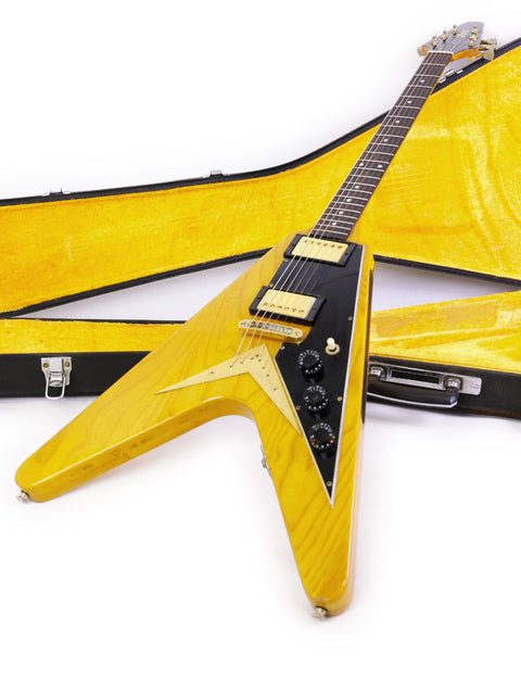 The yellow Ibanez 2387CT Rocket Roll Sr. Flying V guitar is seen in its case on the floor, representing a piece of music history.