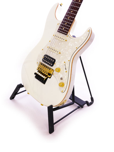 Tom Anderson Drop Top Classic guitar in white, elegantly positioned on a stand with a contrasting black base.

