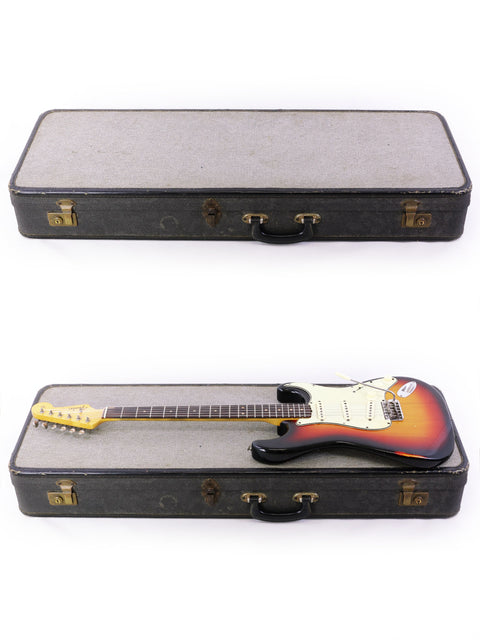 Two guitars, one being a 1964 Fender L Series Stratocaster, displayed in a case with a simple white background.