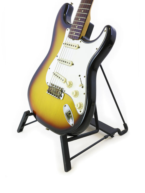 Vintage 1965 Fender Stratocaster guitar elegantly positioned on a stand with a bright white background.