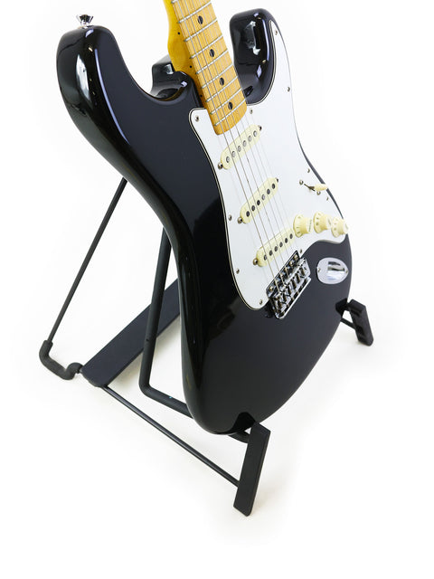 Vintage 1981 Fender Stratocaster guitar in black, resting on a stand with a striking white background for contrast.