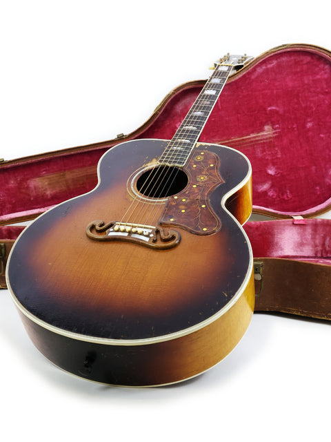 Vintage Gibson J-200 guitar from 1954, displayed with its case and a guitar pick, representing timeless musical heritage.