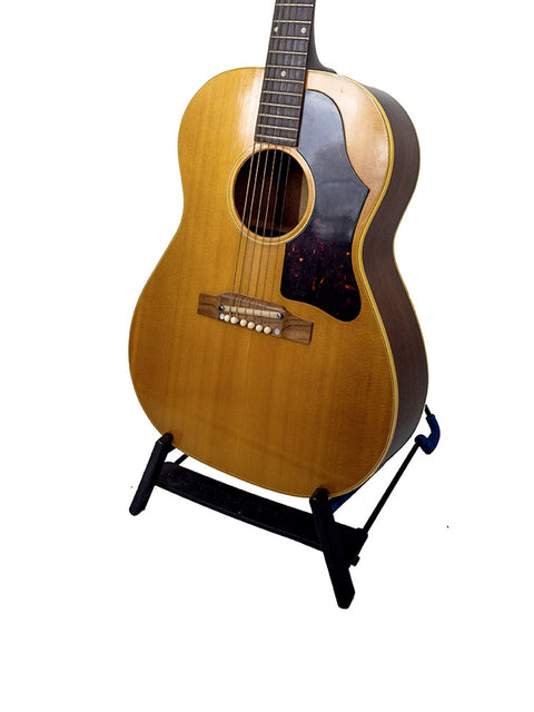 Vintage Gibson LG-3 Acoustic guitar from 1962 resting on a stand against a plain white background.