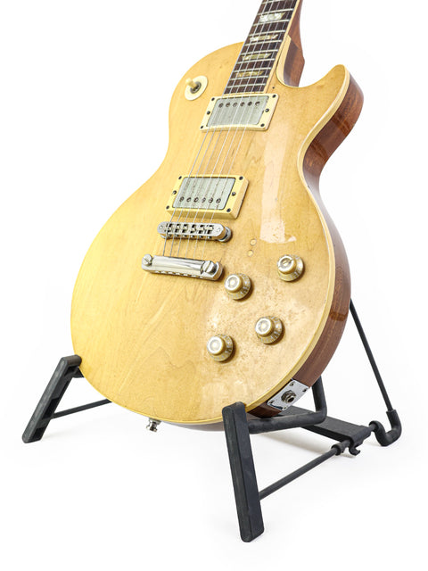 Vintage Gibson Les Paul Deluxe guitar from 1973 resting on a stand, highlighted by a bright white background.