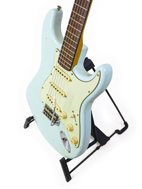 White electric guitar, a Fender Custom Shop '59 Stratocaster, displayed on a black stand, highlighting its craftsmanship.
