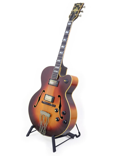 Yamaha AE1200 guitar, featuring a striking sunburst finish, stands gracefully on a stand, a gem from 1982.