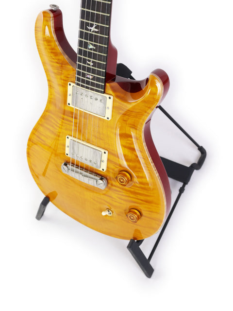 Yellow-bodied PRS Custom 22 guitar from 2005, displayed on a sleek black stand, highlighting its unique design.
