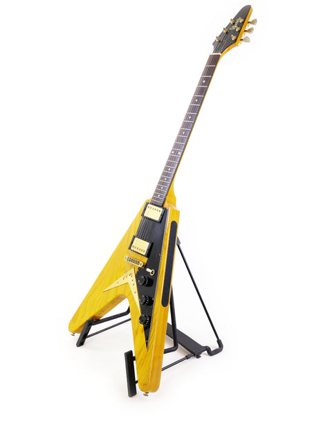 Yellow Ibanez 2387CT Rocket Roll Sr. Flying V guitar displayed on a stand with a clean white backdrop.