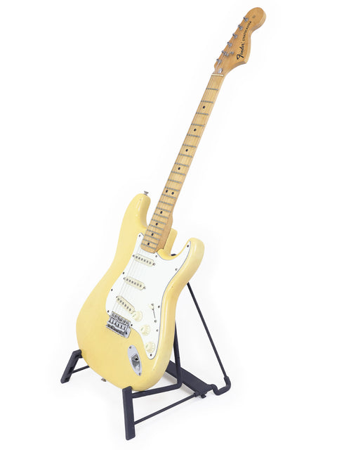 Yellow vintage Fender Stratocaster guitar from 1954, elegantly positioned on a stand with a white backdrop.
