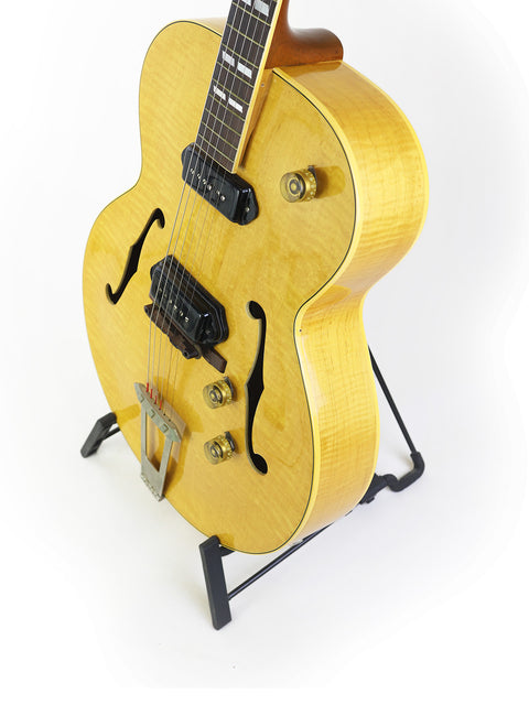 Yellow vintage Gibson ES-300 guitar on a stand, set against a bright white background.