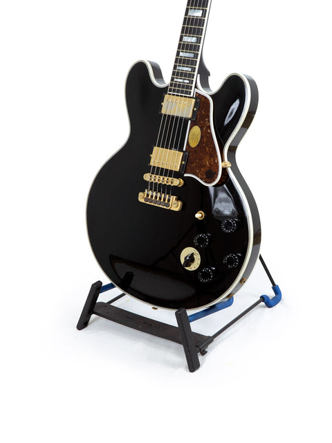 black guitar on a stand with a blue base, featuring signatures of BB King and Eric Clapton, model Gibson Lucille, USA 2000.