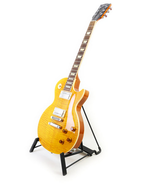 bright yellow Gibson Les Paul Standard guitar displayed on a stand, set against a simple white backdrop for emphasis.

