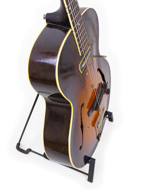 classic 1938 Gibson ES-150 guitar elegantly positioned on a stand with a white backdrop.