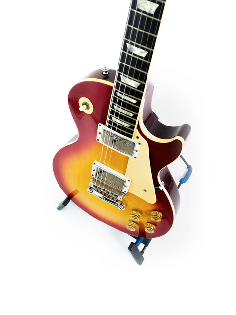red Gibson Les Paul Standard guitar from 1998 rests on a stand against a clean white background.
