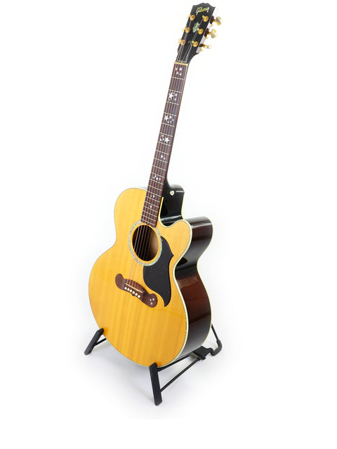 vibrant yellow acoustic guitar, the Gibson J-180EC from 2001, elegantly positioned on a stand for display.