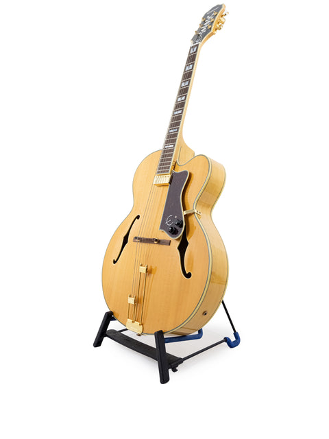 vintage 1965 Epiphone Coronet guitar displayed on a stand, set against a stark white backdrop.
