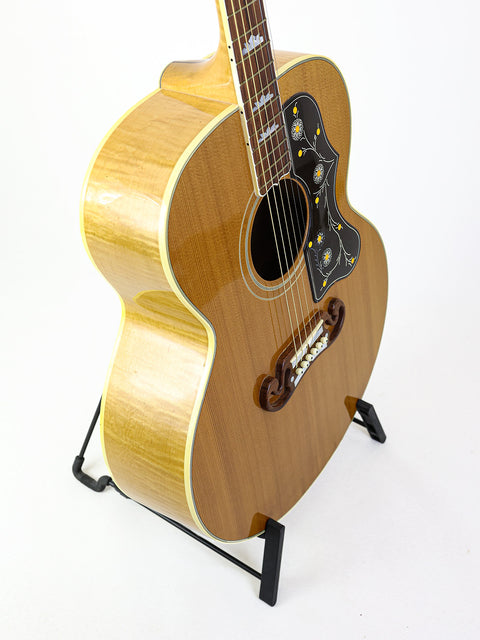 white background highlights a Gibson SJ-200 guitar from 2001, elegantly positioned on a stand.