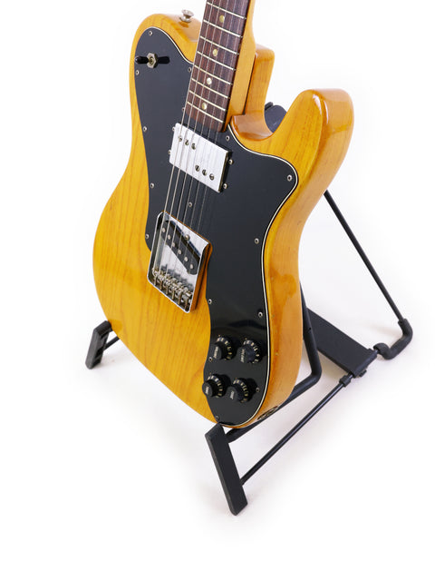  yellow 1977 Fender Telecaster Custom guitar resting on a stand, adorned with a stylish black strap for added flair.
